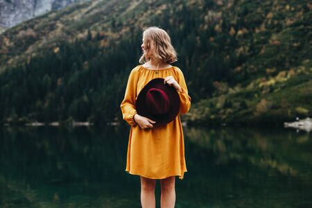 Magnetic girl in the yellow dress with red hat in her hands by stunning lake Morskie oko in mountainsの写真素材