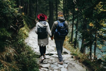 Lovely couple travelling together in the mountains, walking around the lake Morskie oko in Tatry. Stunning view. Girl in yellow sweater and red hat with grey backpackの写真素材