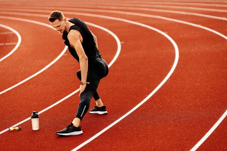 Young handsome man doing stretching before running in the stadiumの写真素材