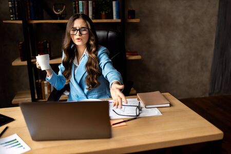 Angry young woman dressed in blue jacket sitting at her workplace