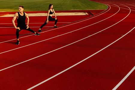 Young men and women doing stretching before running at the stadium.の写真素材