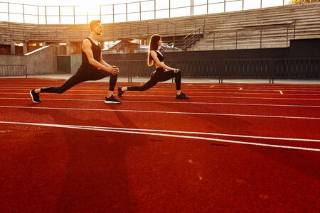 Young athletic man and athletic woman warm up before running in the stadium