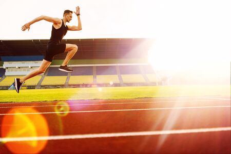 Young handsome athlete running at the stadium at sunset