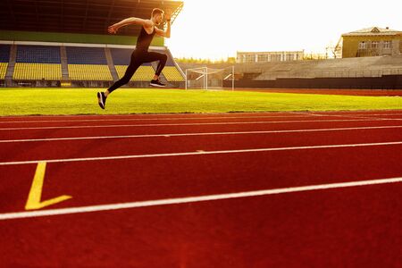 Young handsome athlete running at the stadium at sunset