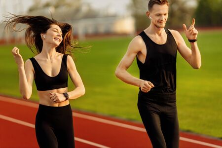 Young man and woman running wearing black sport suits in modern stadium.の写真素材