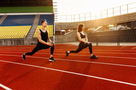 Young athletic man and athletic woman warm up before running in the stadiumの写真素材