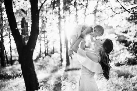 Beautiful woman with baby girl walking at the park, lovely mother kissing adorable daughter, caring parent lifts in air cute toddler, enjoy happy family moments, weekend outdoors, parenthood concept. High quality photoの写真素材