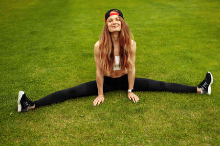 Overjoyed athletic woman practice flexibility at the stadium, smilie, doing stretching, recommends healthy lifestyle, daily workout concept. High quality photoの写真素材