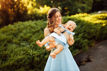 Overjoyed mother play with adorable daughter at the park, pretty woman hold baby girl in caring arms, smile, enjoy happy family moments, weekend outdoors, parenthood conceptの写真素材