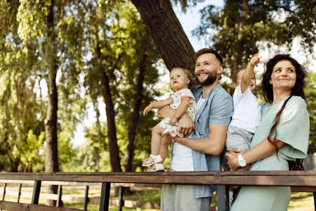 Happy family with little kids at the park, beautiful mother hold in arms joyful son, adorable...