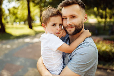 Portrait of handsome man with little boy at the park, lovely son sitting on fathers arms, smiling, dad and toddler spend time together, enjoy tender family moments, parenthood conceptの写真素材