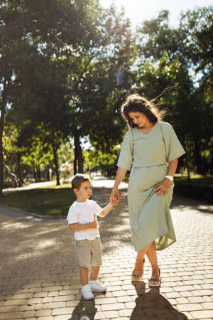 Lovely woman with little boy walking at the park, cute son hold mother hand, smiling, mom and toddler spend time together, enjoy happy family moments, parenting conceptの写真素材