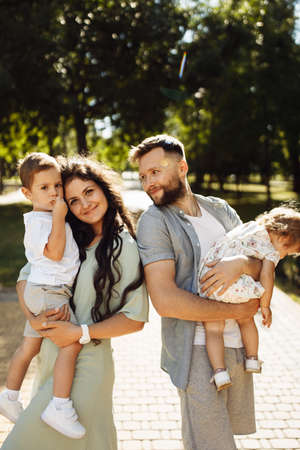 Overjoyed family with little kids at the park, caring dad hold in arms adorable daughter, joyful son sitting on mother hands, smiling, enjoy parenting, childhood conceptの写真素材