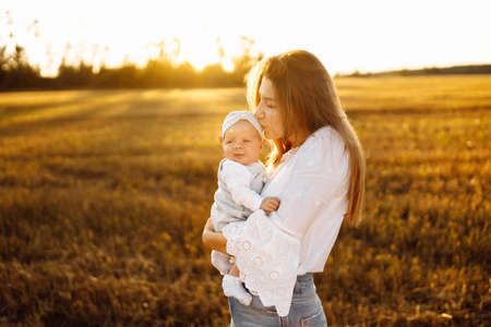 Adorable mother with beautiful little daughter at the field, pretty woman hold cute newborn baby in...