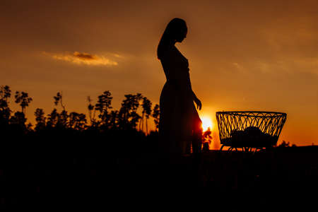 Lovely woman near tiny bed with newborn baby girl at the field, happy mom spend time with little...