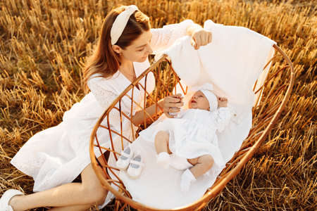 Wonderful mother with little daughter at the field, newborn baby girl laying in the tiny bed, lovely...