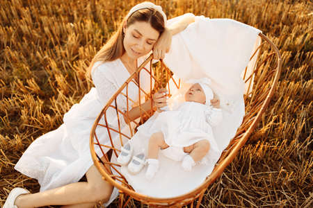 Gorgeous woman near tiny bed with beautiful newborn baby girl at the field, loving mother take care...