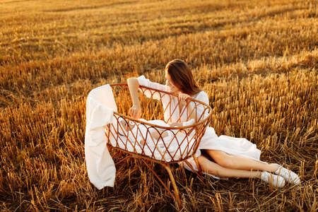 Adorable woman sitting near tiny bed with lovely newborn baby girl at the field, caring mother enjoy...