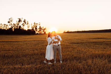 Happy parents with lovely newborn baby girl walking at the field, caring dad hold in arms little daughter, beautiful mother hugging handsome father, smiling, young family concept. High quality photoの写真素材