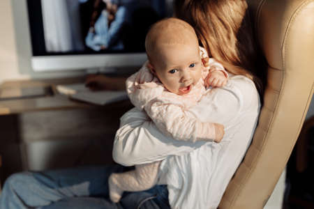 Portrait of adorable baby girl in caring arms of young mother, loving mom making notes, write down...