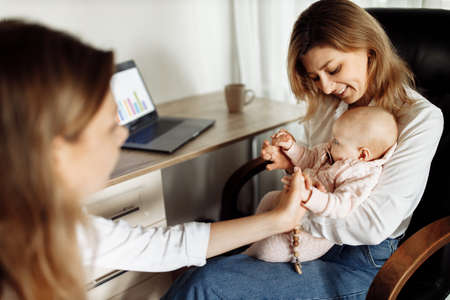 Happy woman take a break from work to spend time with little daughter, young mother working from home, while loving grandmother babysit newborn baby girl, young mother working home. High quality photoの写真素材