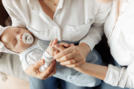 Close up of hands of three generations, middle aged woman shows care and support to her adult daughter, loving grandmother hold in arms sleeping baby girl, childcare concept. High quality photoの写真素材