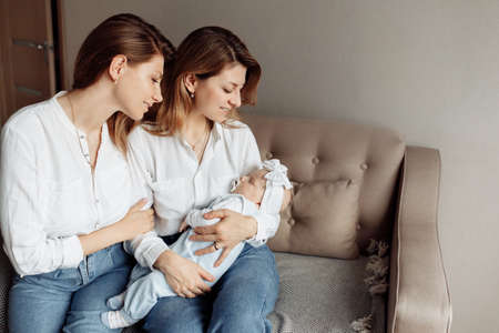 Lovely middle aged woman with her adult daughter sit at the sofa, caring grandmother hold in arms...