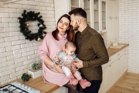 Beautiful young family with little daughter at the kitchen, decorate the house for Christmas...