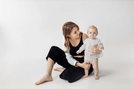 Lovely stylish mother is holding adorable little daughter and looking gently at her. Beautiful cute...