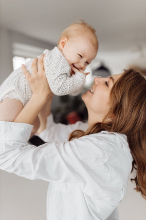 Joyful mother lift her adorable little daughter in the air, playing together. Beautiful woman with...