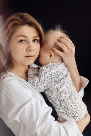 Portrait of young stylish woman with her adorable baby girl in the studio. Happy beautiful mother gently hugging cute little daughter, looking at the camera. High quality photoの写真素材