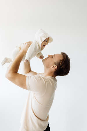 Happy dad holds the baby in his arms, lifting her up. The adorable little daughter is overjoyed. Play together in a room on a white background. Family concept. High quality photoの写真素材