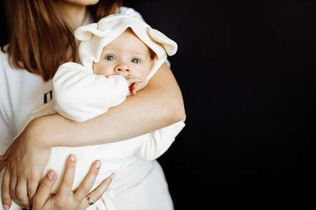 A young mother lovingly holds the baby in her arms, enjoying the moment. Baby cute posing for a photo in the studio, on a black background. High quality photoの写真素材
