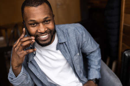 Close-up portrait of happy African American young man having fun talking on cell phone in office....