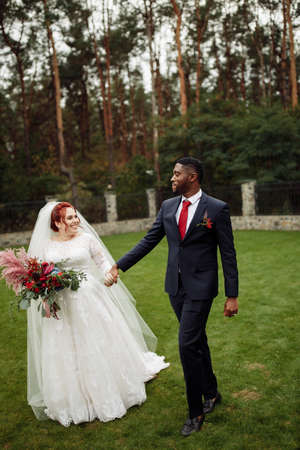 Joyful couple walking at the park, handsome African American man with lovely white woman on wedding day, beautiful bride with charming groom enjoy happy moment, marriage concept. High quality photoの写真素材