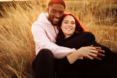 Adorable couple lay at the field, attractive husband gently hug adorable wife, overjoyed woman smiling, happy family spend time together, walking, weekends outdoors concept. High quality photoの写真素材