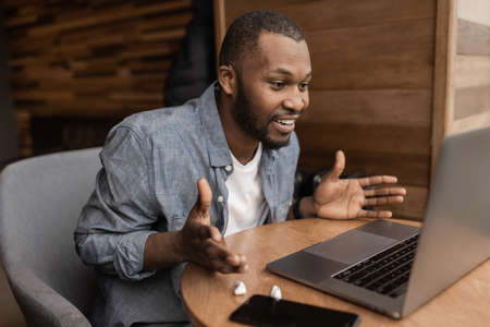 African american freelancer is using laptop, having a video conference. Handsome businessman talking with coworkers on online meeting, discuss corporate project, concept of remote workの写真素材