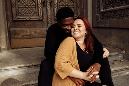 Adorable couple cuddling near the house, walking at the city, charming African American husband gently hug beautiful wife, overjoyed woman smiling, tender moments concept. High quality photoの写真素材
