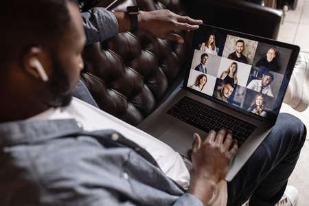 Side view. Young African American business man making video call looking at laptop screen, confident positive young coach teaching remote lesson, businessman participating in online conference.の写真素材