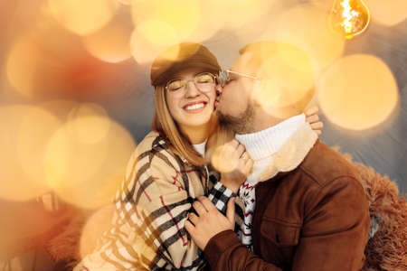 Adorable couple hugging, smiling, happy man kiss at cheek beautiful woman, caring husband spend cozy winter holidays with beautiful wife, festive mood, Christmas concept. High quality photoの写真素材