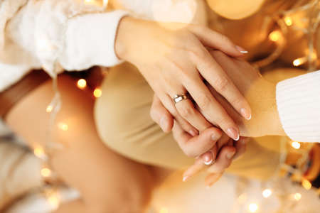 Close up of beautiful wife hold a hand of caring husband, near light garland, handsome man spend cozy winter holidays with adorable woman, festive mood, Christmas concept. High quality photoの写真素材