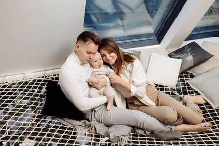 Beautiful parents with adorable baby girl sitting at home, smiling, young family with little daughter enjoy happy moments, cozy winter holidays, vacations, parenthood concept. High quality photoの写真素材