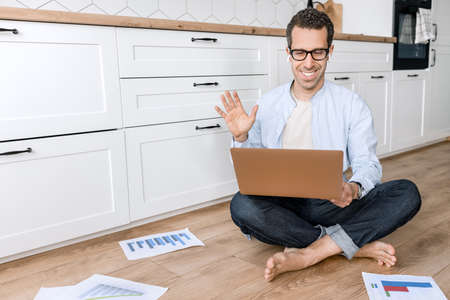Happy successful businessman is using laptop, waving to colleagues at video meeting, smile. Stylish...
