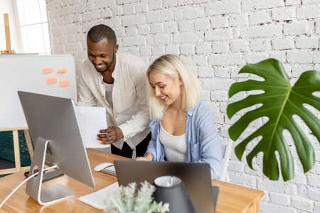 Joyful multiethnic employees working together in modern office, smiling, doing paperwork. Happy successful colleagues discussing new project or strategy for the company, partnership conceptの写真素材