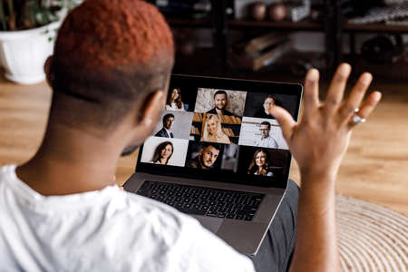 Back view of african american male freelancer waving hello to coworkers on video meeting, using...