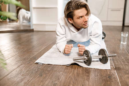 Concentrated male is working out at home in the morning, doing plank pose. Athletic caucasian man is training, exercising to keep good shape, motivates to healthy lifestyle, wellness conceptの写真素材