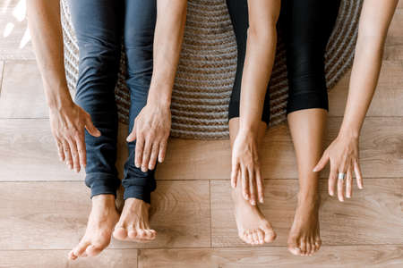 Close up of barefoot couple sitting and warming up in sportswear on the floor at home before online work. Young man and woman stretching isolated on the carpet together. High quality photoの写真素材