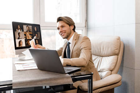 Smiling successful man businessman in business suite sitting on armchair with laptop in luxury...