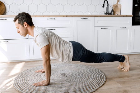 Home Workout. Sporty man working hard and making push up exercise on the floor of his kitchen before...