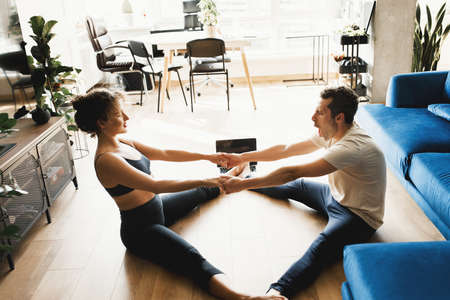 Back view couple stretching watching fitness video tutorial online on laptop. Fit man and woman...